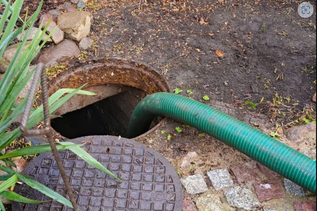 Septic tank being serviced with a green hose leading into the open tank.